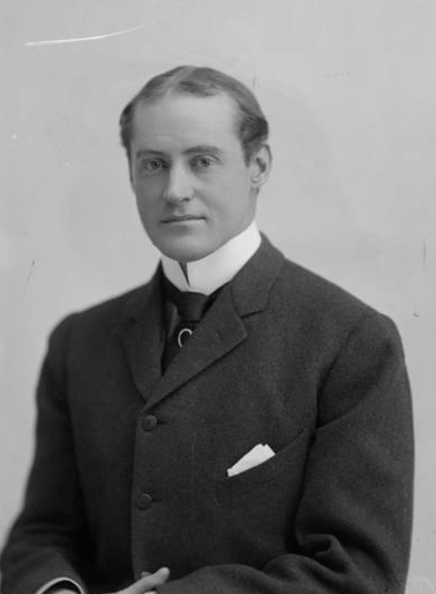 Irving Brokaw in a black and white photo sitting down in a 1920s era black suit.