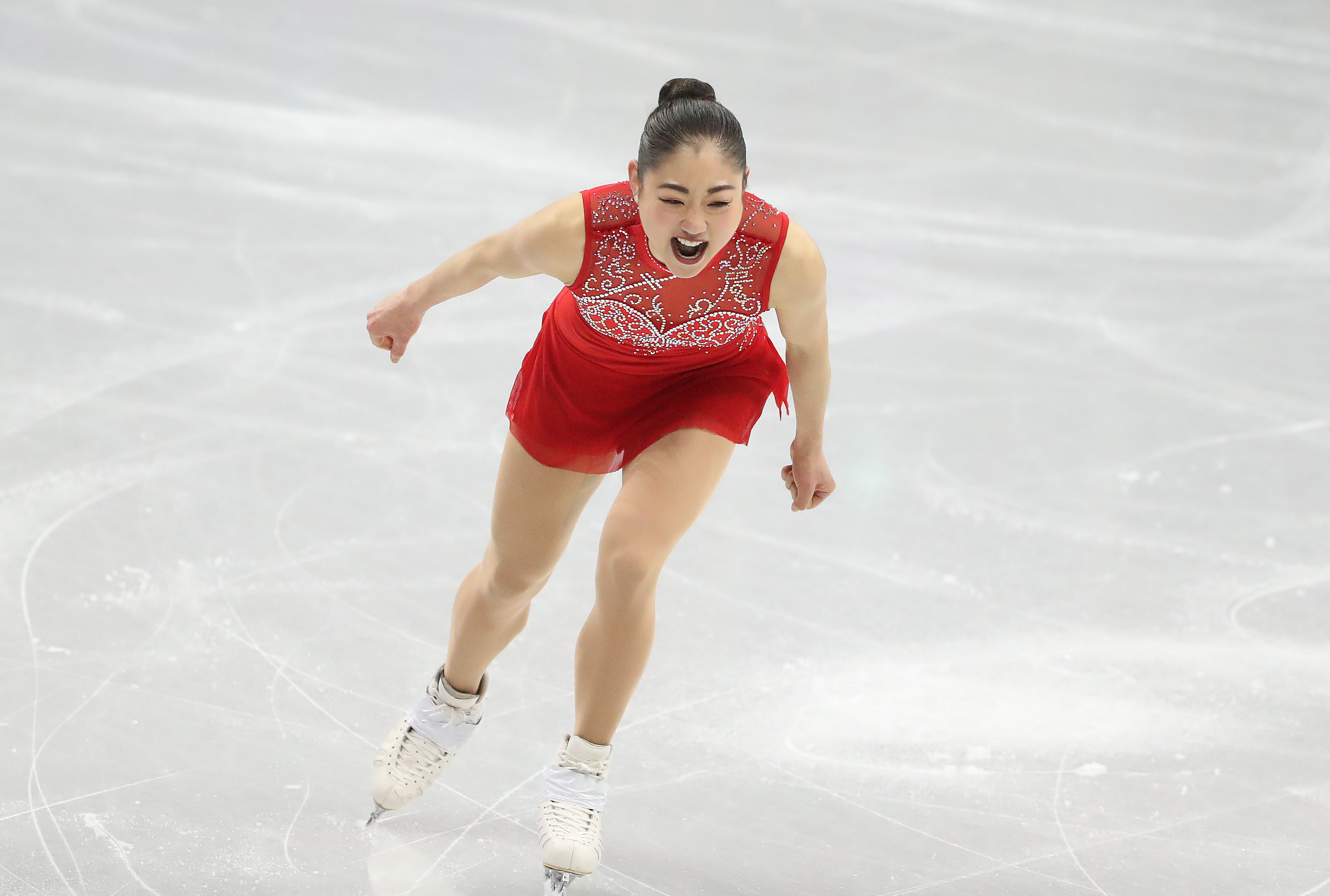 Mirai Nagasu in a red dress celebrates on the ice after landing a triple Axel.