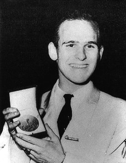 Dick Button shows his gold medal to the camera while smiling.