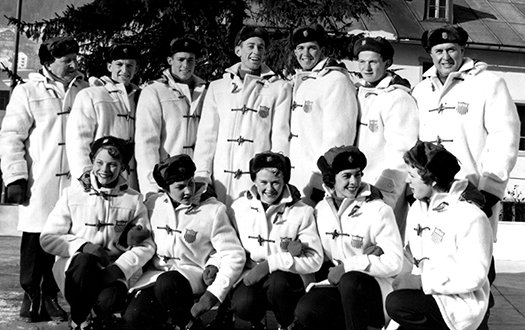 1956 U.S. Olympic Figure Skating Team, wearing white jackets, poses for the camera in an outdoor setting.