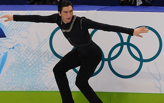 Evan Lysacek performs a backwards crossover in front of the Olympic rings.