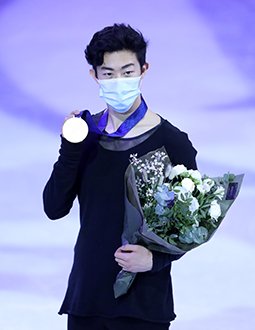 Nathan Chen poses with his gold medal and flowers while wearing a mask at the 2021 World Championships