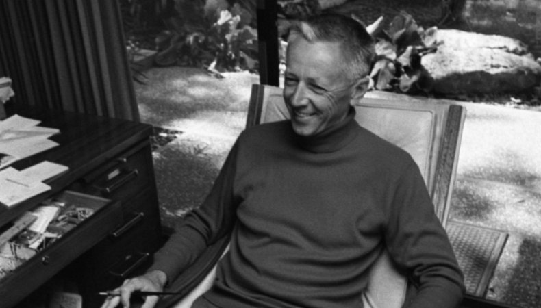 Charles Schulz smiles, sitting in a chair.