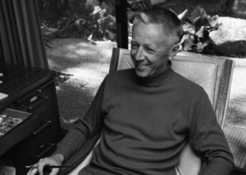 Charles Schulz smiles, sitting in a chair.