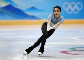 Karen Chen on practice ice at the 2022 Olympics, with the rings on the boards behind her.