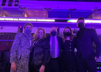 A group of old and young officials in business clothing and masks under purple lighting in an ice arena.