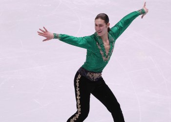 Jason Brown with long brown hair and his signature Riverdance green shirt on the ice.