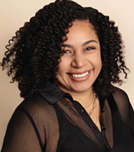 Headshot of Cassandra Lock. Cassandra is a young African American woman with black curly hair. She is wearing a black collared shirt and a gold necklace