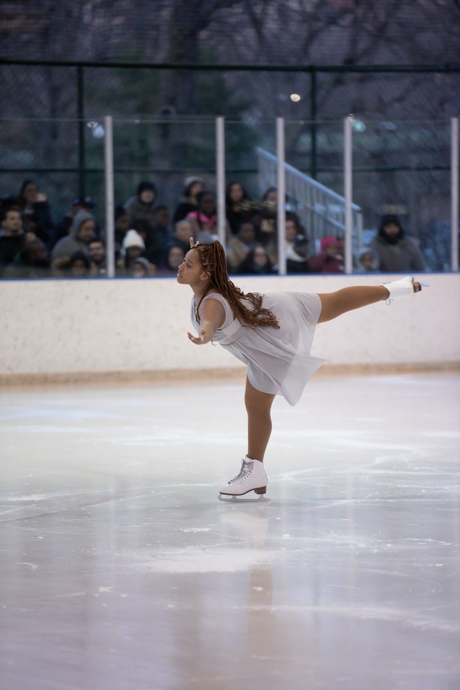 Dressed in white and performing a spiral, a member of Figure Skating in Harlem performs in front of a crowd.