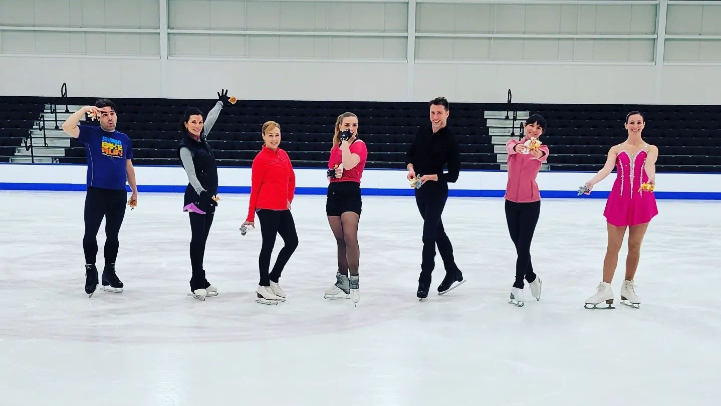 A group of skaters line up on the ice in costumes holding stuffed animals.