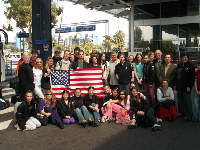 Group photo of Imagica of Boston as they arrive in France for the Grand Prix International des Aigles competition. They are holding a large American flag. 