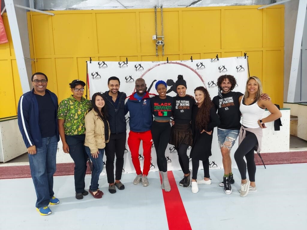 Group of skaters standing together to pose for a photo. They are all standing in front of a Diversify Ice backdrop. Two are wearing a shirt that says, "The Future of Skating is Colorful," and another is wearing a Black History Month tshirt