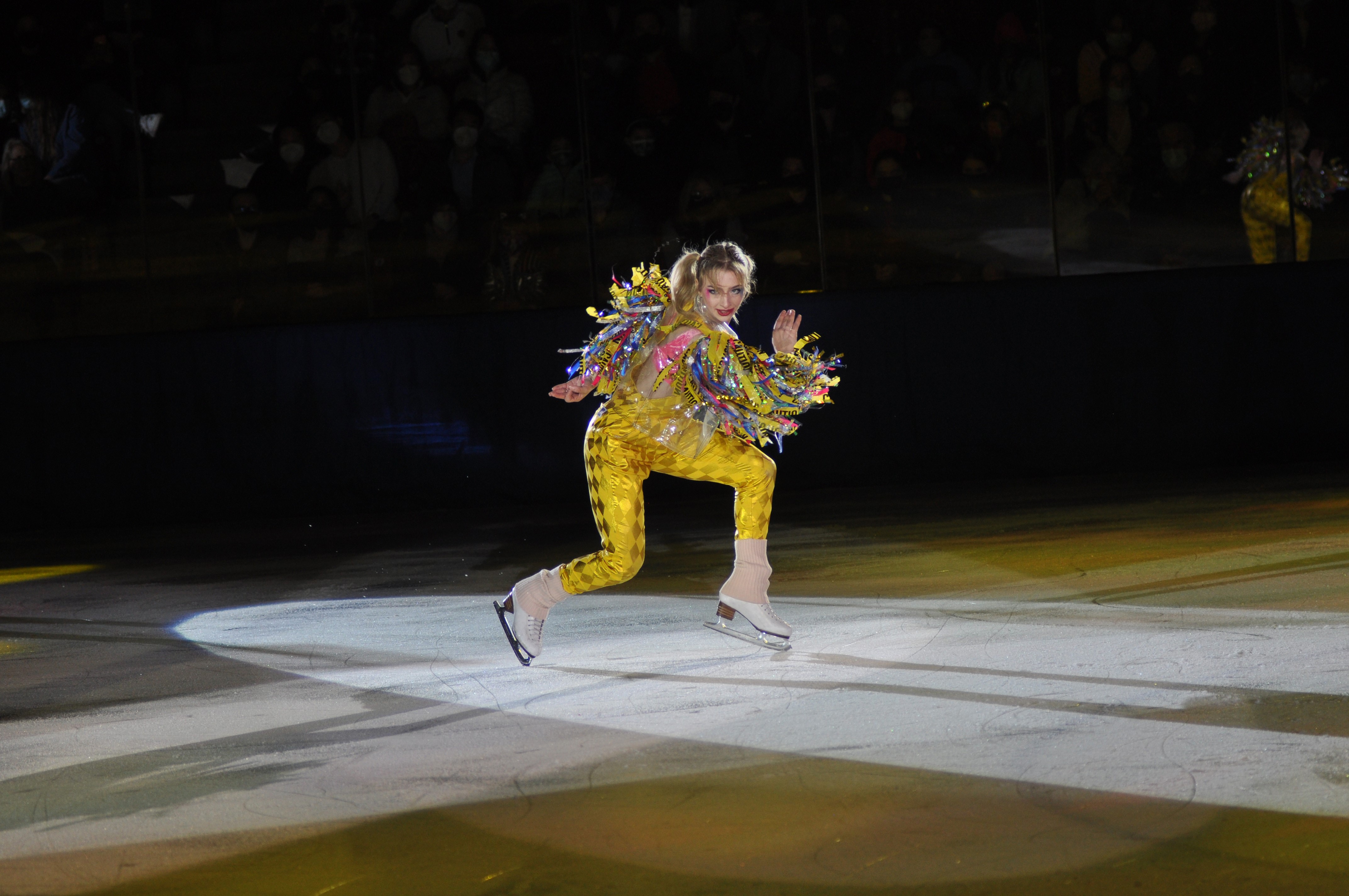 Amber Glenn wears caution tape and yellow pants while skating under a spotlight.