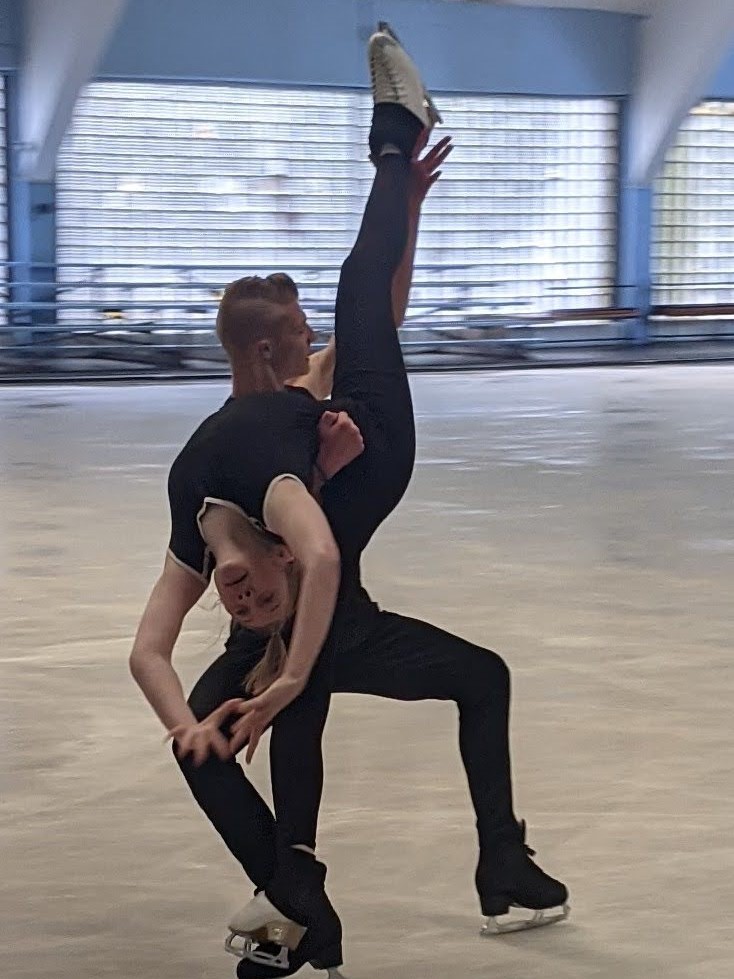 Cianin and Brysin, dressed in black, work on a lift that has Cianin draped over his shoulder, upside down.