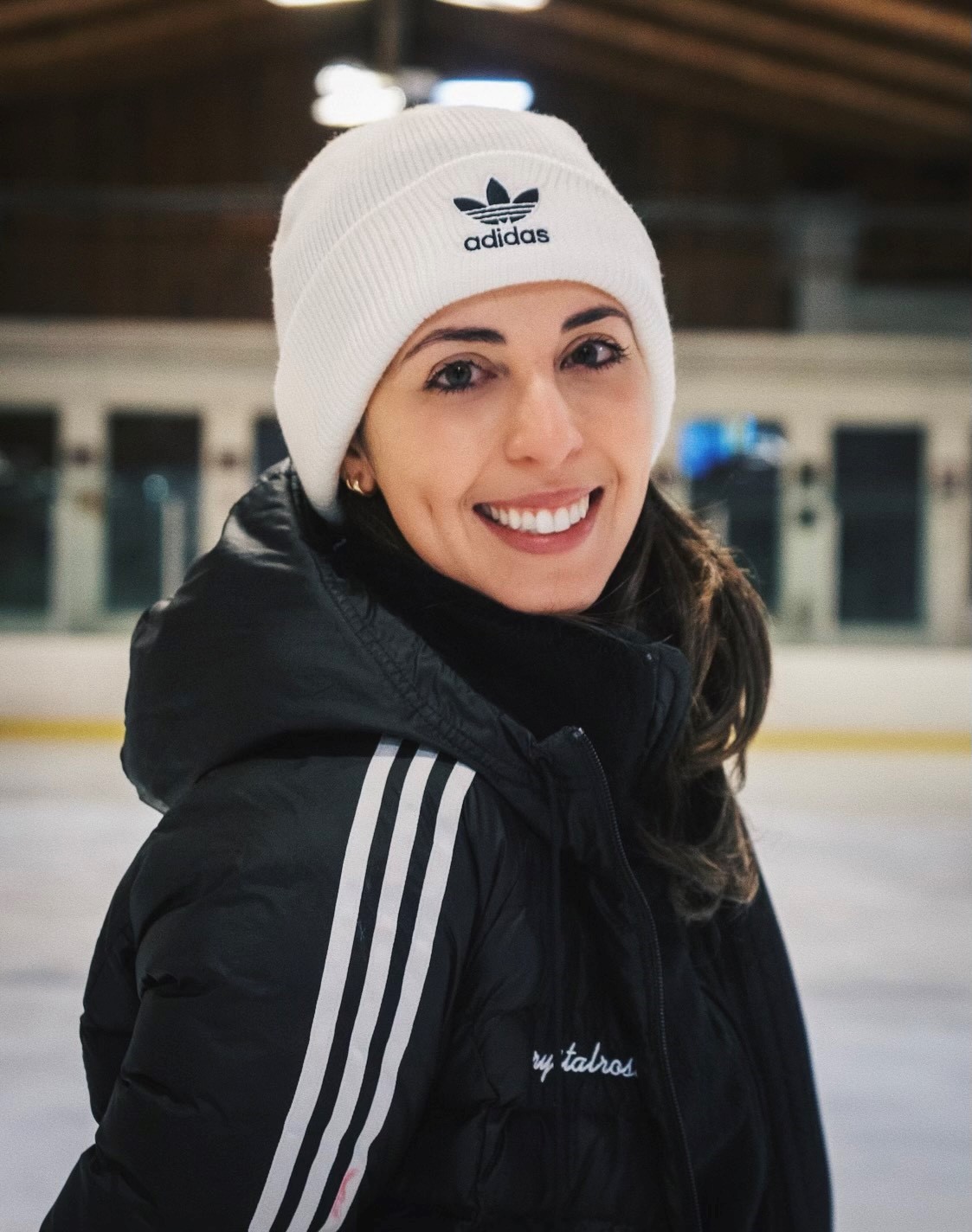 Headshot of a Latina woman weating a black winter jacket and white knit had with the Adidas logo on the front