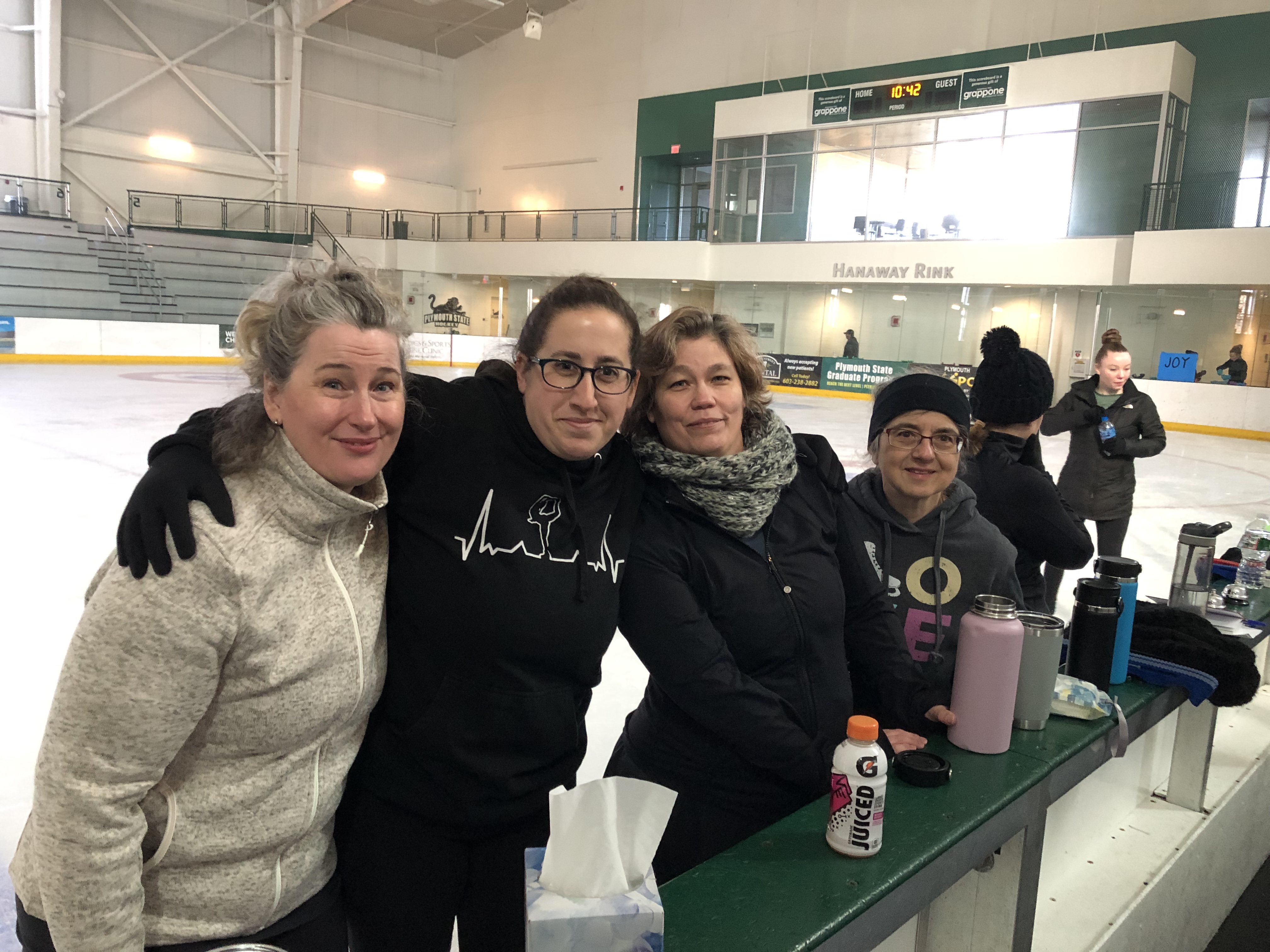 Three adult skaters at the RiverWalk Adult Camp on the ice by the boards.