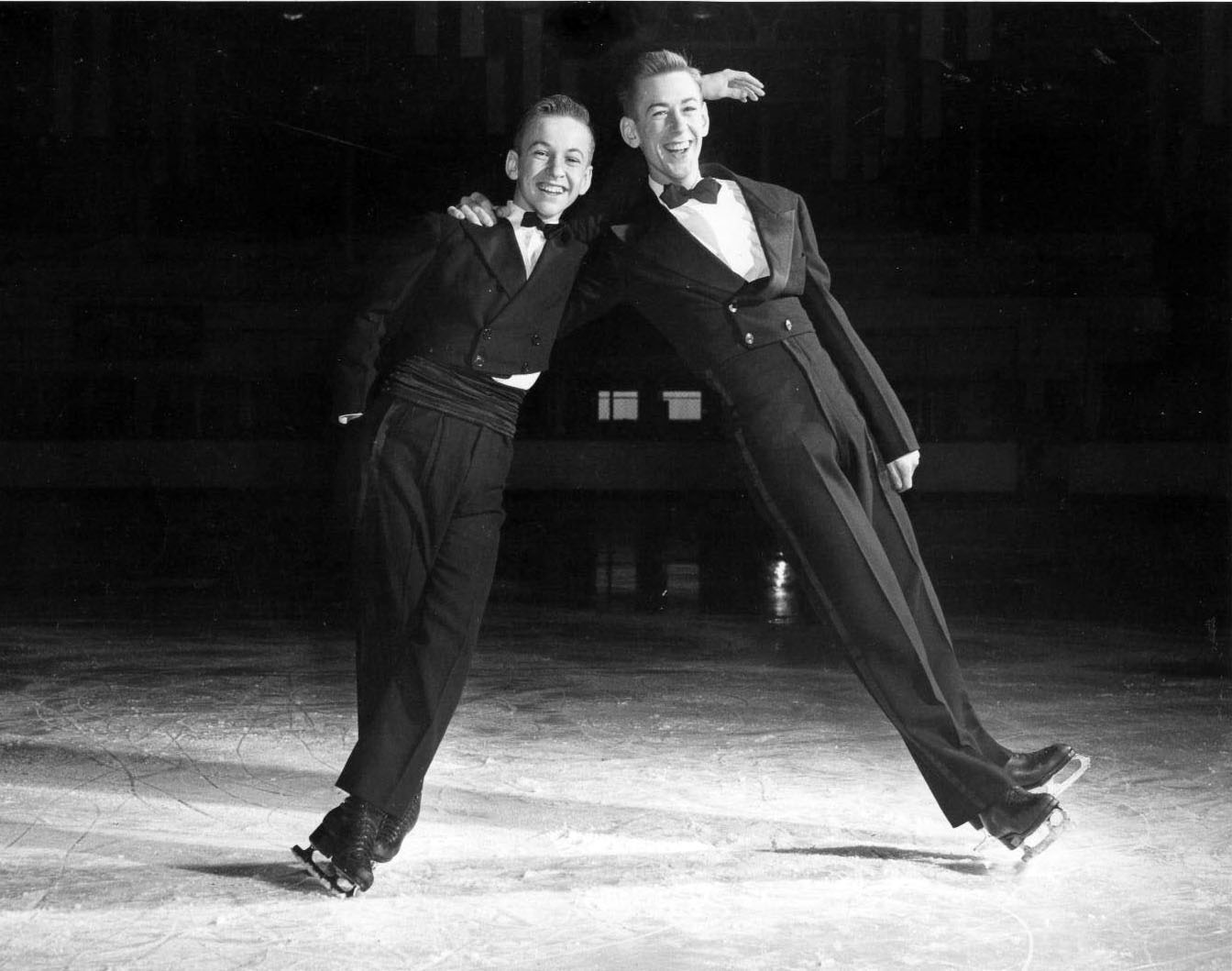 Hayes and David Jenkins, both in suits, on the ice leaning up against each other. Photos is taken in black and white.