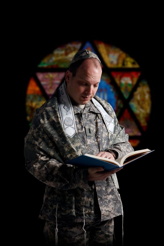 Photo of Mark Getman wearing his Army uniform and a kippah which is typically worn by those that practice judaism. He looks down and reads a book in his hands. 