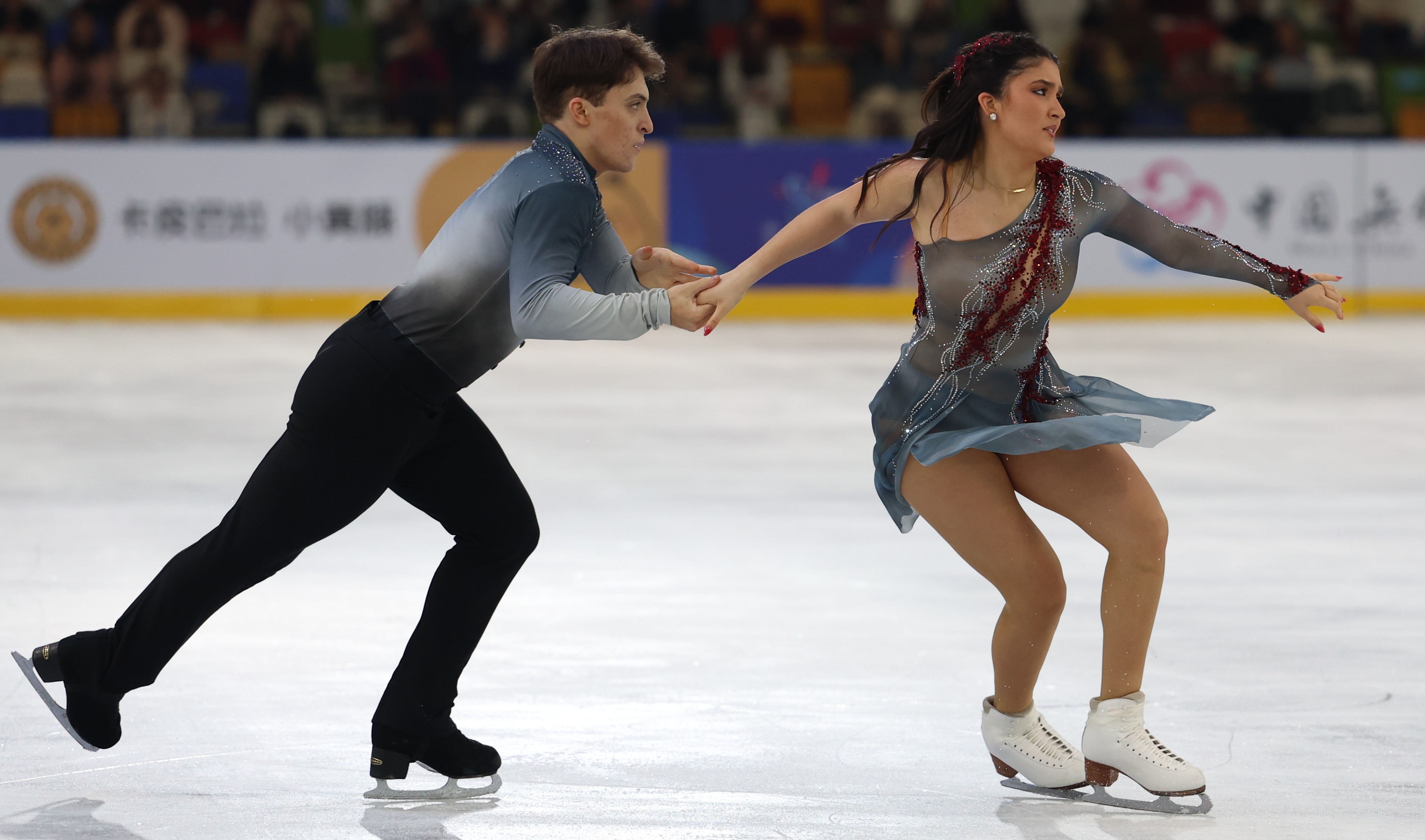 Wearing gray, Ethan Peal takes his partner Elliana Peal by the hand in their free dance to a Pearl Harbor theme.