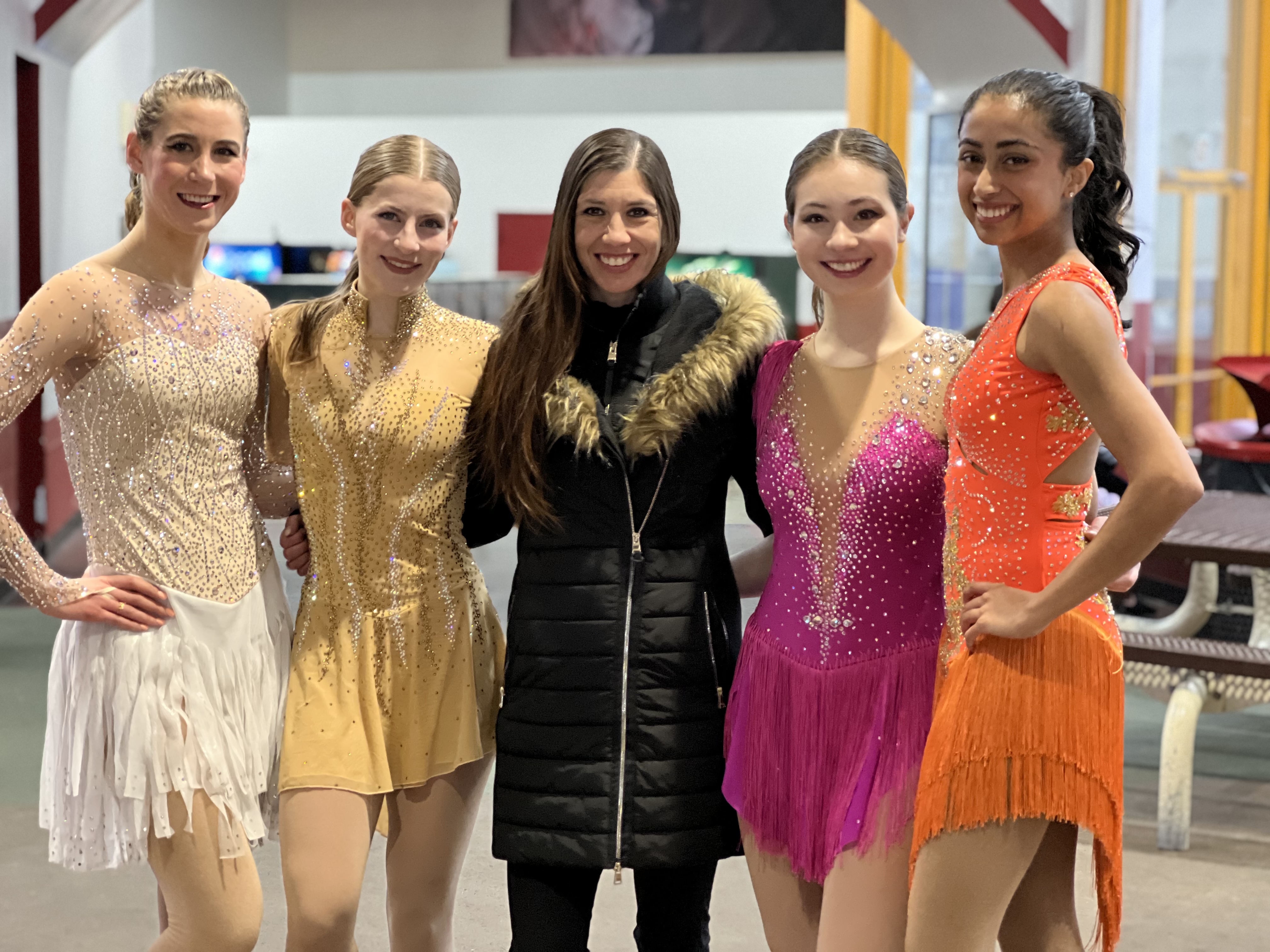 Naomi Lang (center) poses with four skaters wearing various colored skating costumes