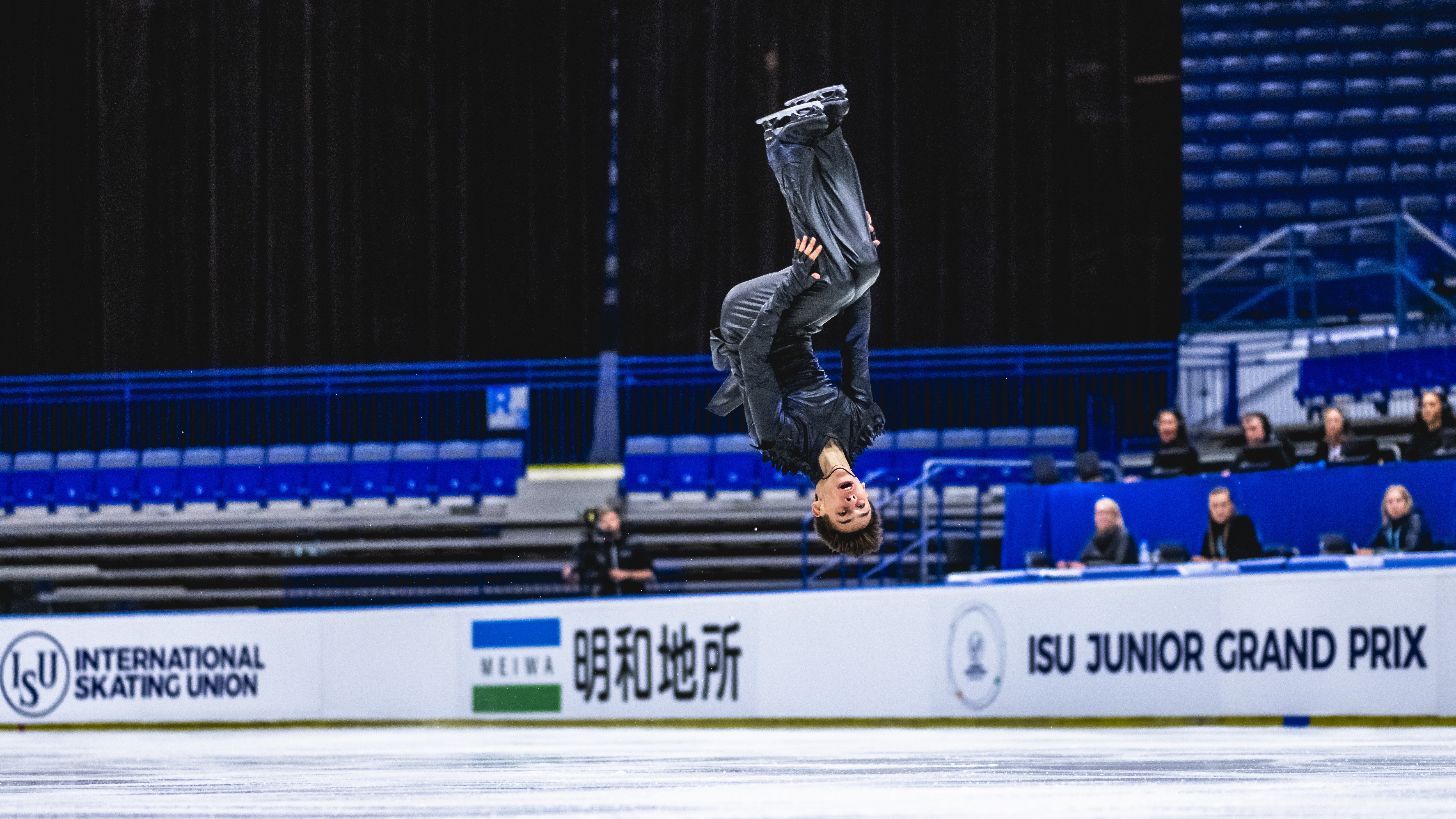 Wearing a totally gray costume, Patrick Blackwell performs a backflip, knees bent, at a Junior Grand Prix event.