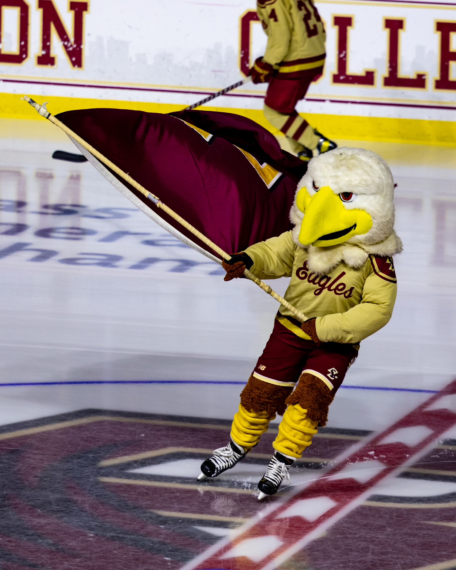 Maddy is dressed in an eagle mascot costume where you can't see her face. She waves a Boston College flag