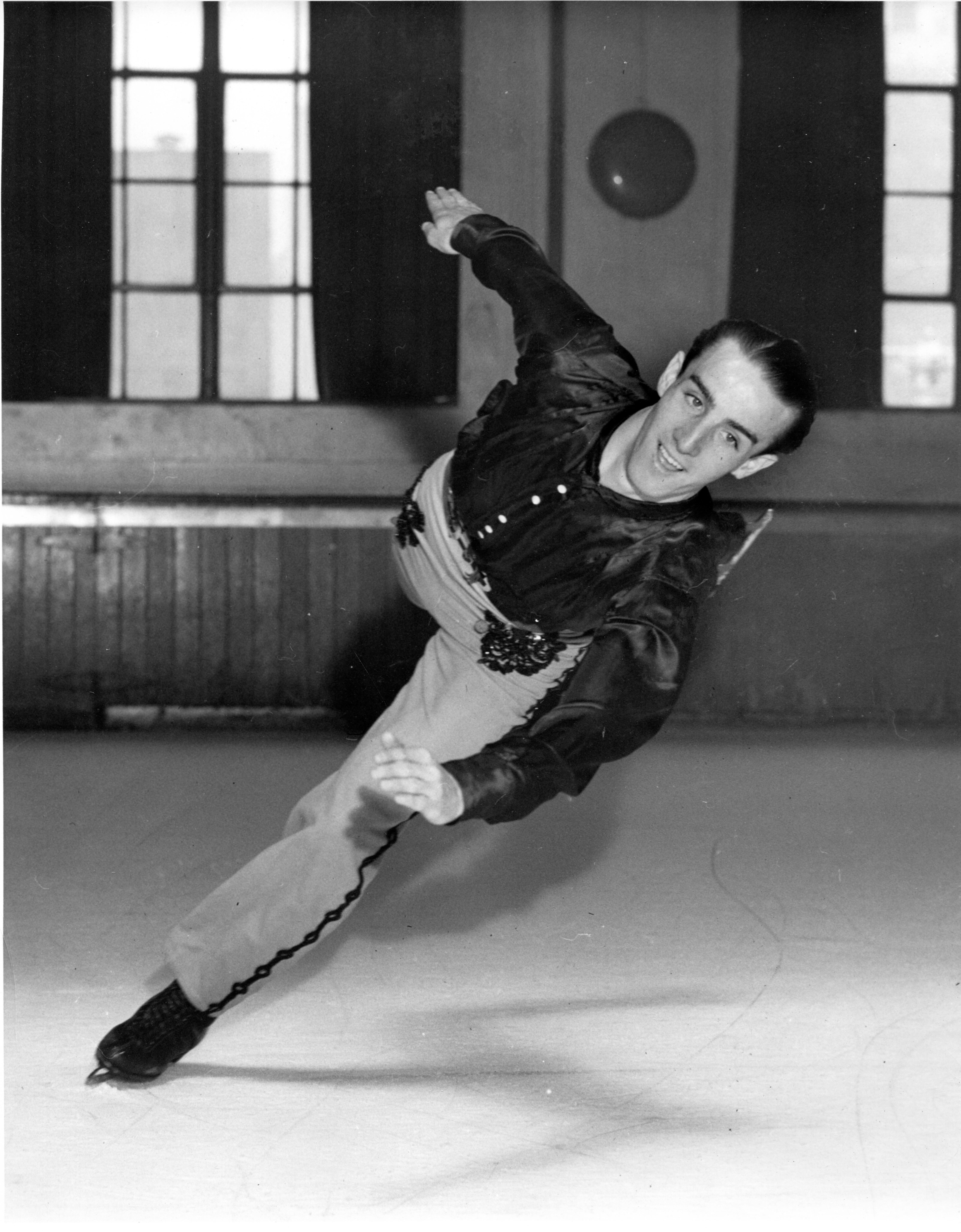 Skippy Baxter leans to the side on one skate with the other extended behind him in a half-spiral.