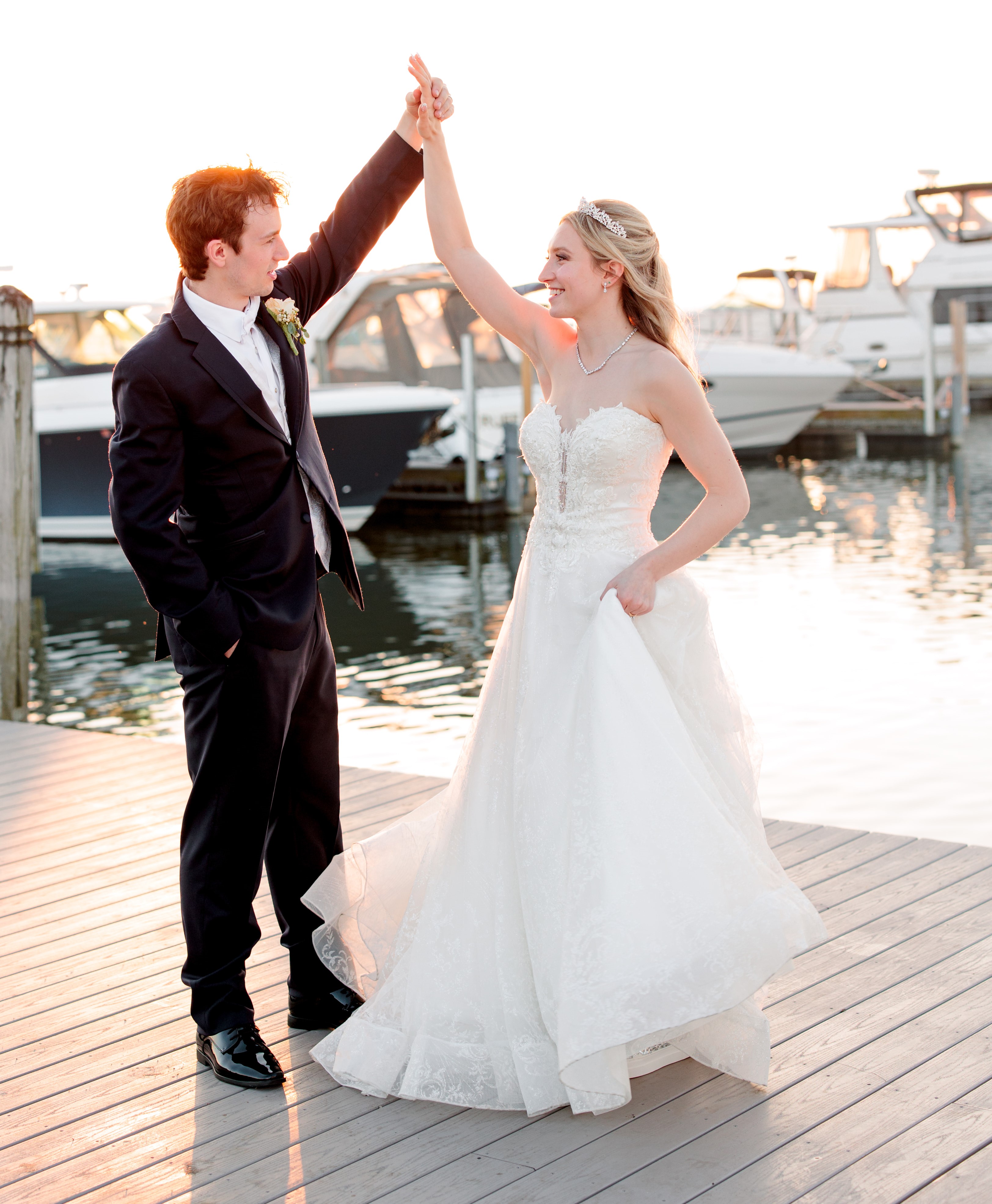 Logan Bye, in a blue tux, spins Eva Pate in her wedding dress. They stand on the dock of a marina.