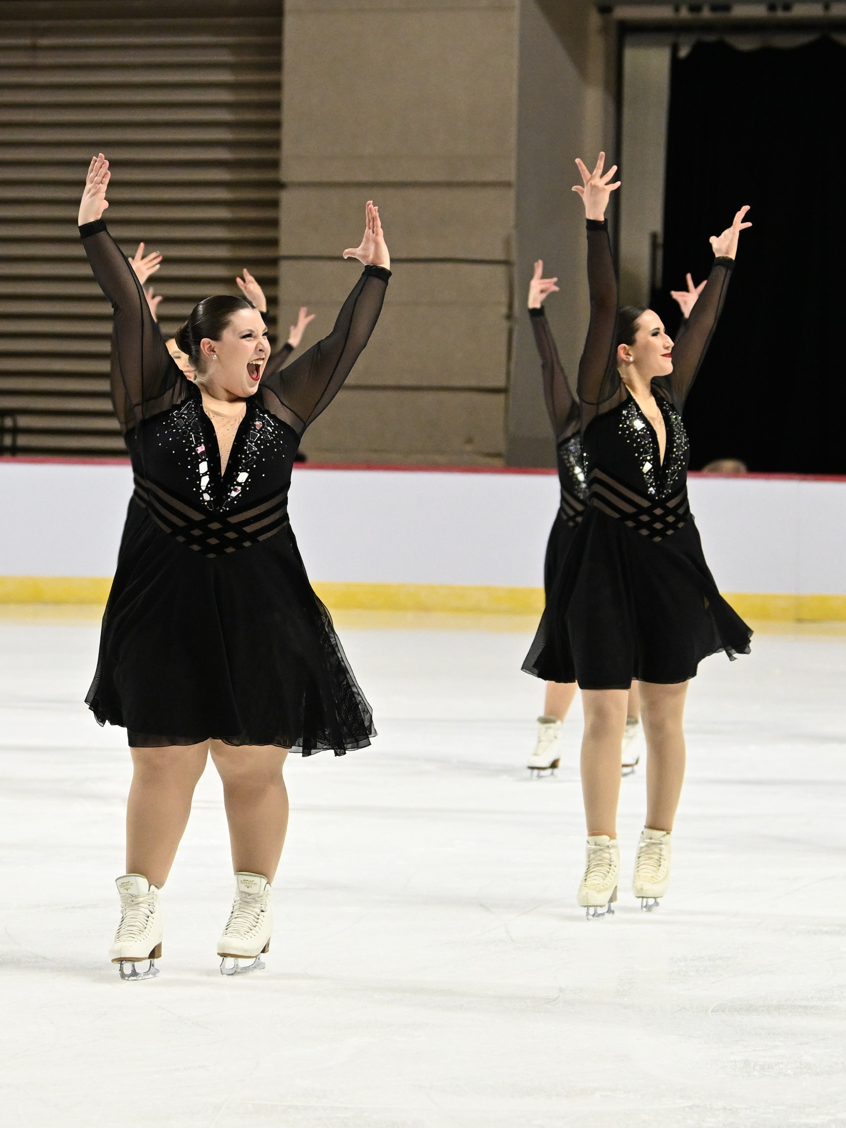 Starlights skate with their arms up wearing matching black skating costumes