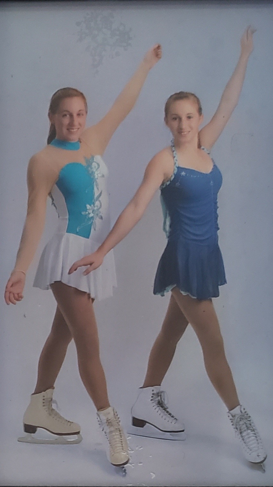 Violet Scibior, right, wearing a blue skating dress, stands with her skating sister, Jacqui, who is wearing a turquoise and white skating dress.