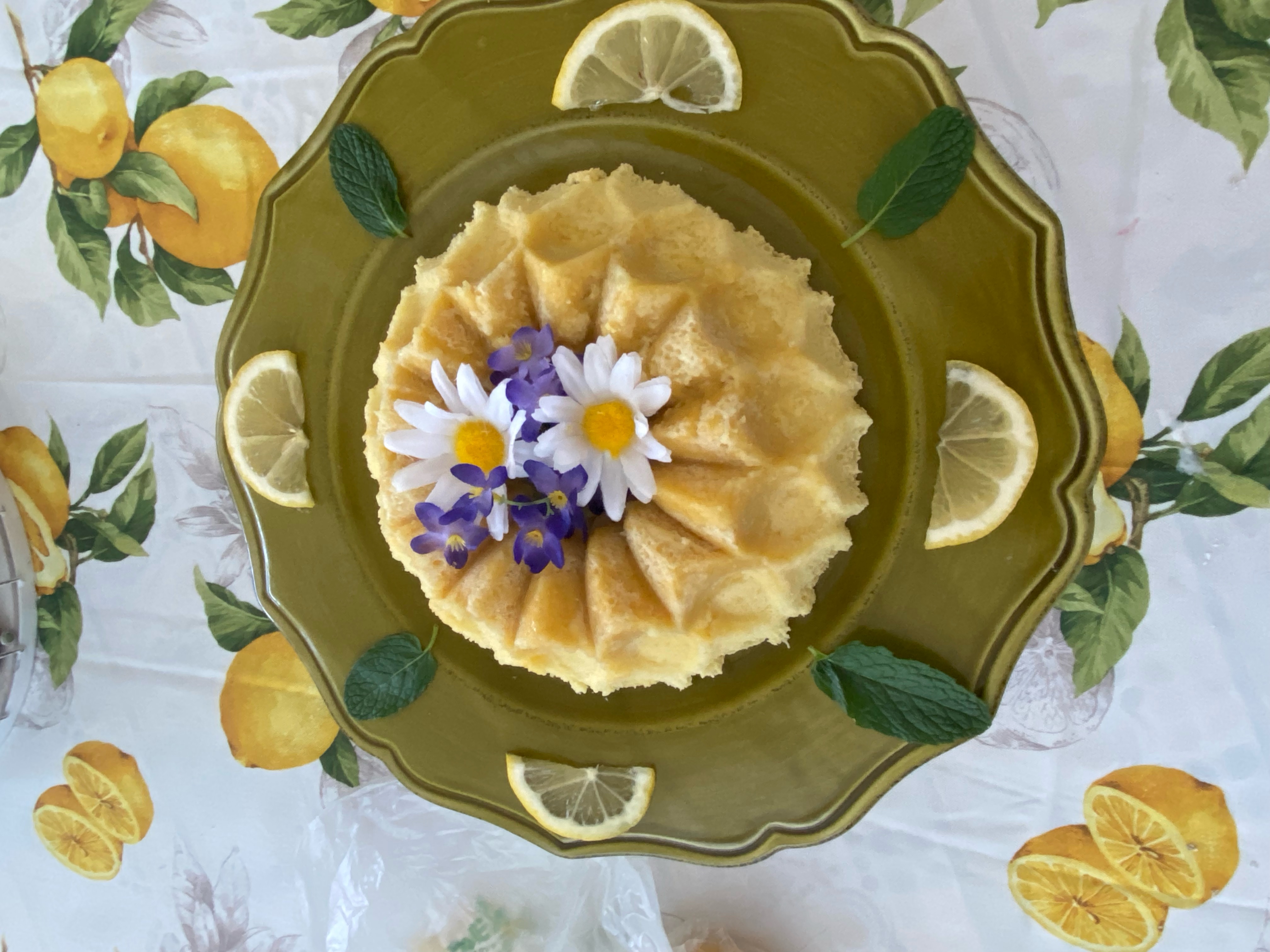 A yellow lemon cake sitting atop a colorful tablecloth.