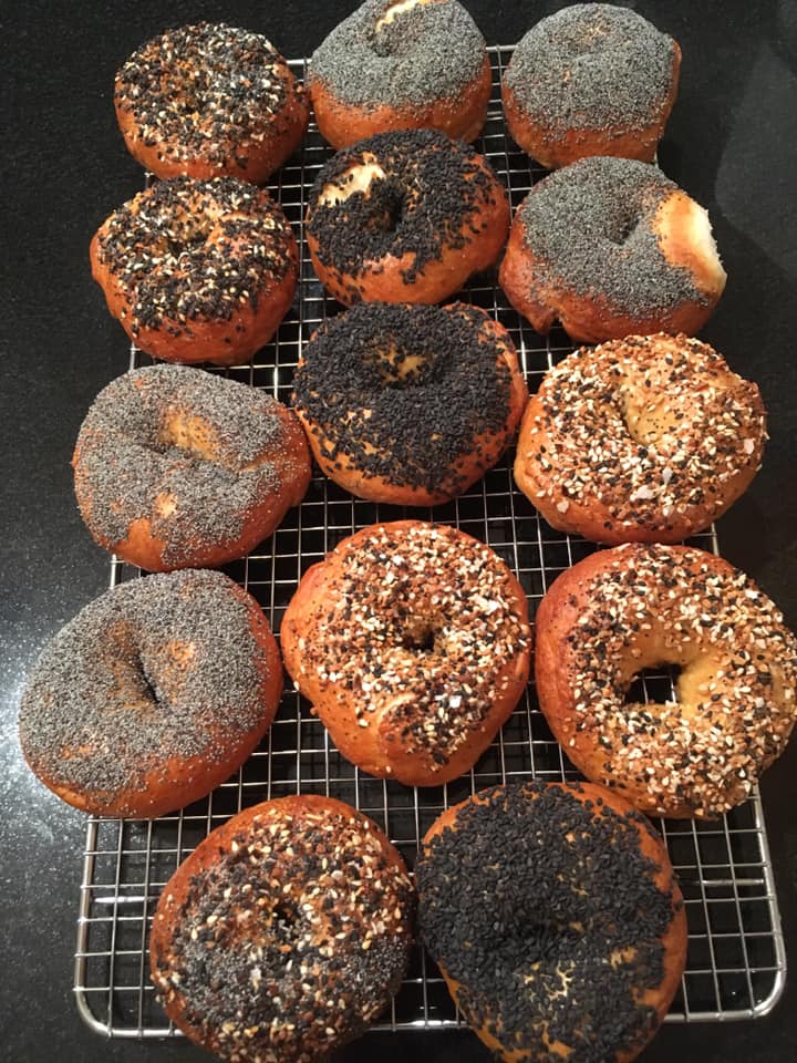 Various types of homemade bagels sitting on a pan.