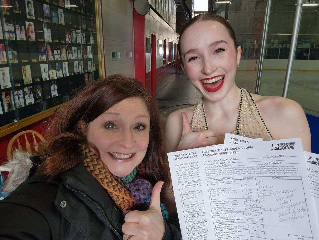 Selfie of Joelle and her coach giving a thumbs up and holding up Simpson's test papers after she passed the free skate test