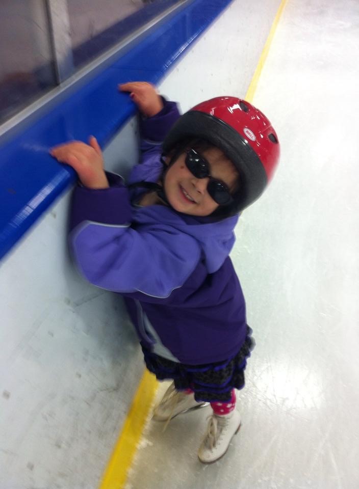 A young Katie Taylor clinging to the rink boards wearing a red helmet and special sunglasses.