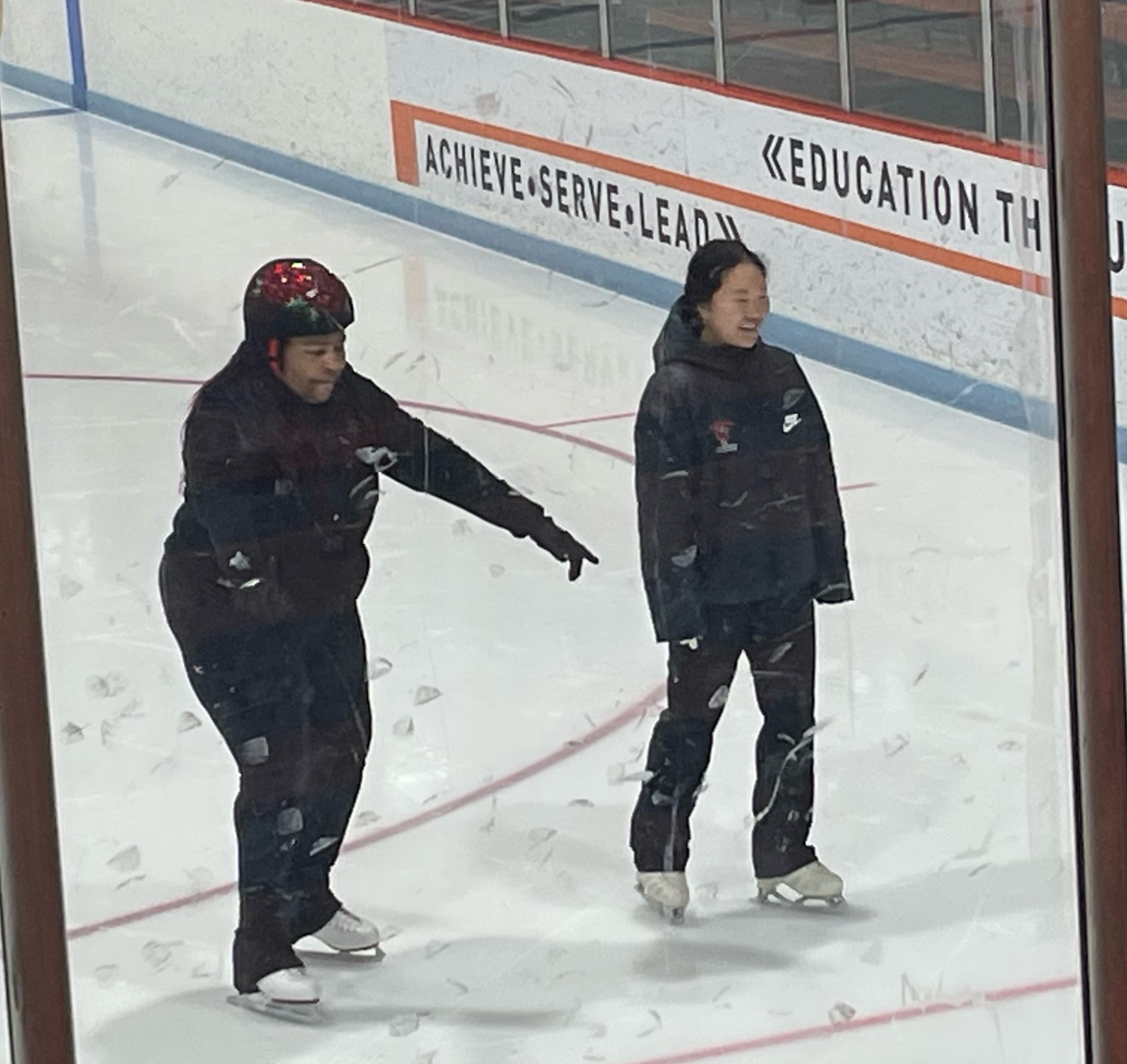 An adaptive skater wearing a red helmet skates with a volunteer wearing a Princeton jacket