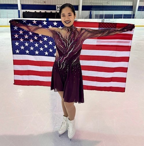 Shin Lei poses holding an American flag wearing a dark red skating costume