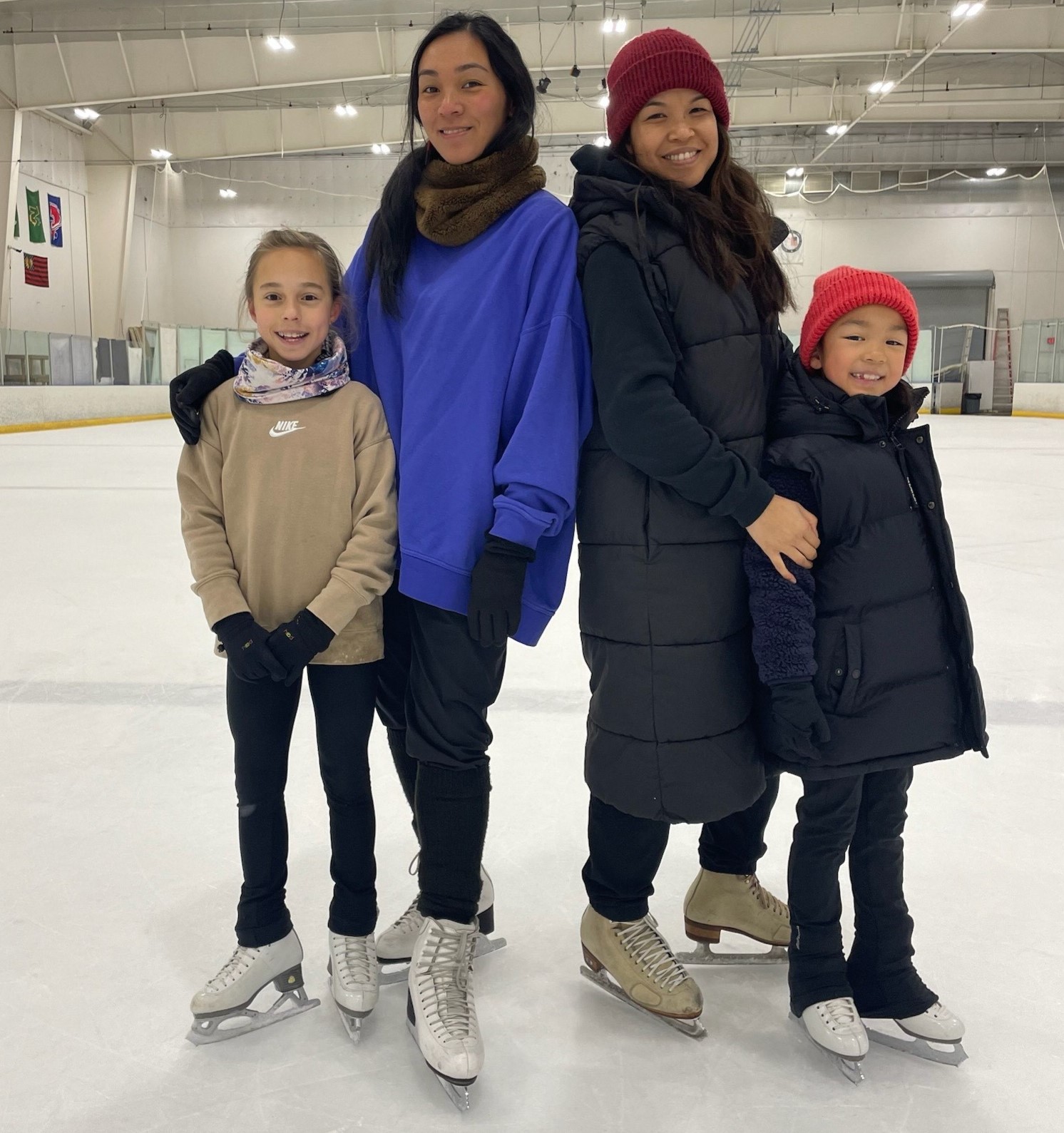 Two women stand with their young skaters on the ice