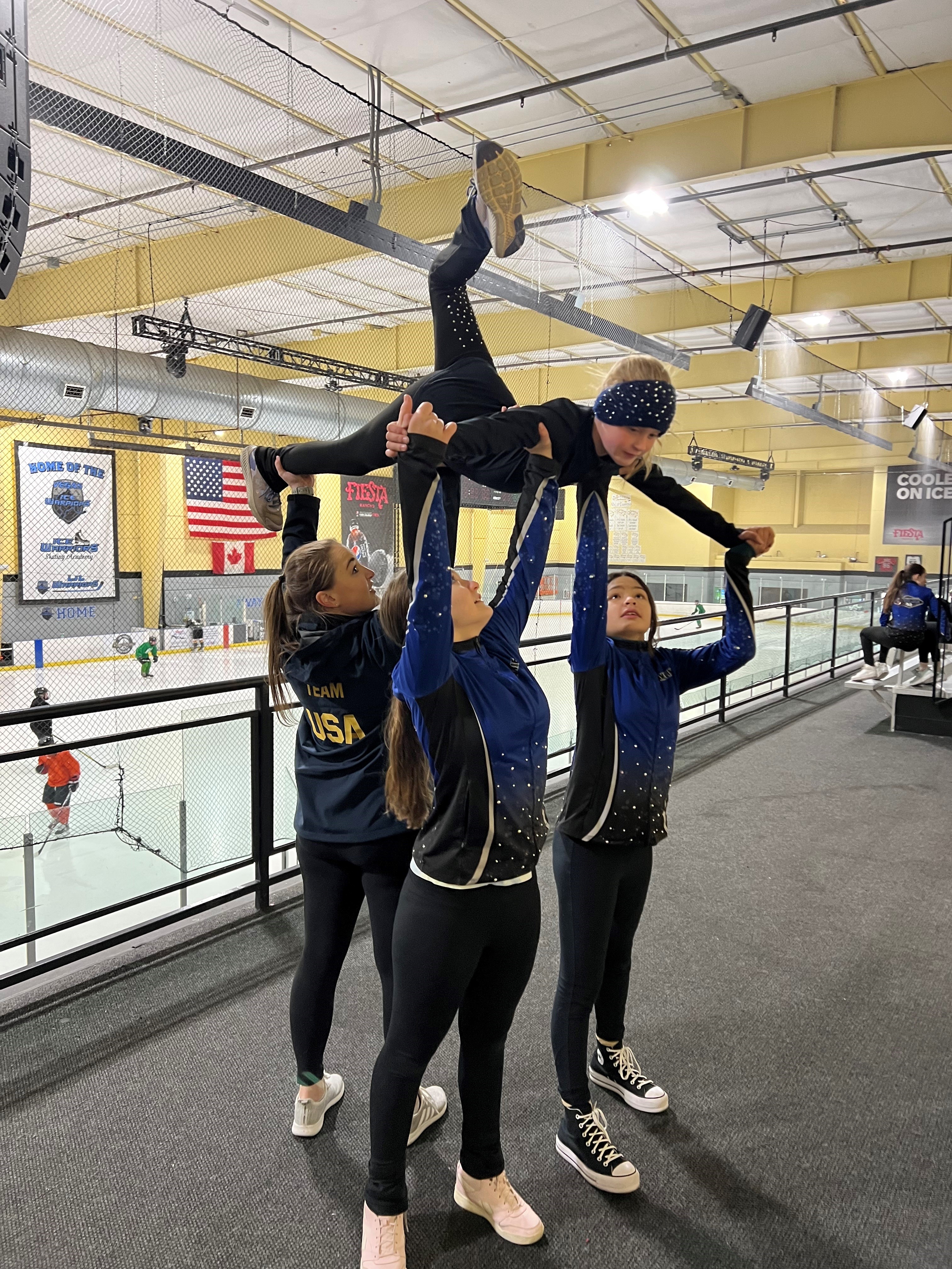 Three female skaters hold up a fourth skater in the air to practice a synchronized skating lift. 