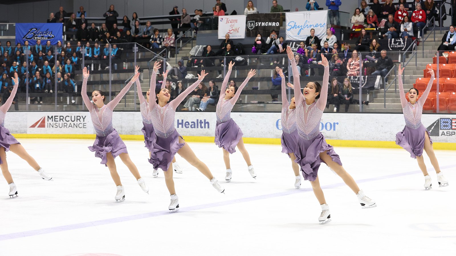 Skyliners junior all skates in their short program wearing matching purple long sleeve skating costumes. They all have their arms raised above their heads and are smiling. 