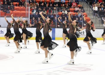 Miami University skates to the left with their left arms raised. They are wearing matching black skating costumes with gold detailing 