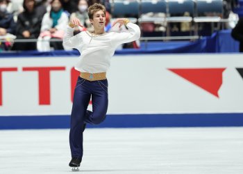 Wearing a white top, tan waistband and blue pants, Andrew Torgashev dazzles the crowd at the NHK Trophy.