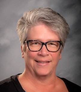 Headshot of a Caucasian woman smiling. She has short grey hair and she is wearing glasses and a black shirt